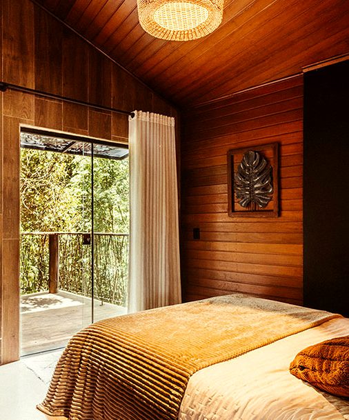 An upper room with a gold bedcover and glass doors open to green canopy