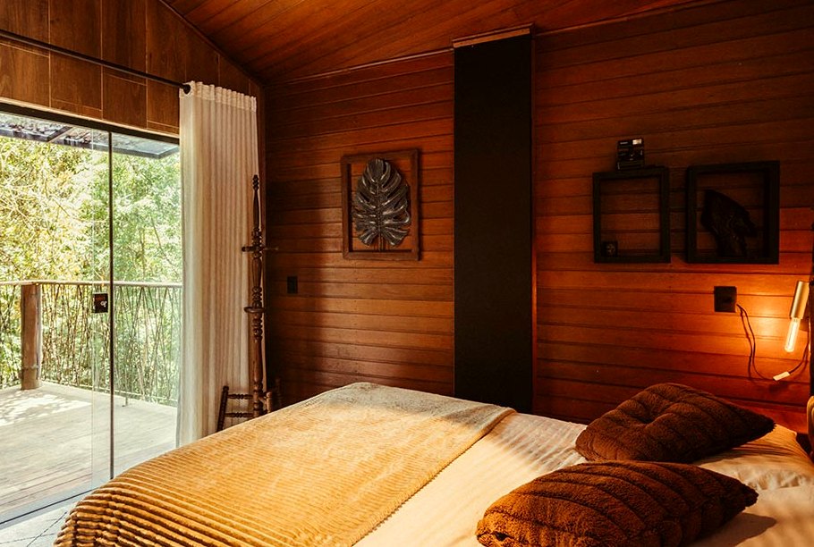 Bed facing open sliding doors onto a timber verandah with rainforest beyond